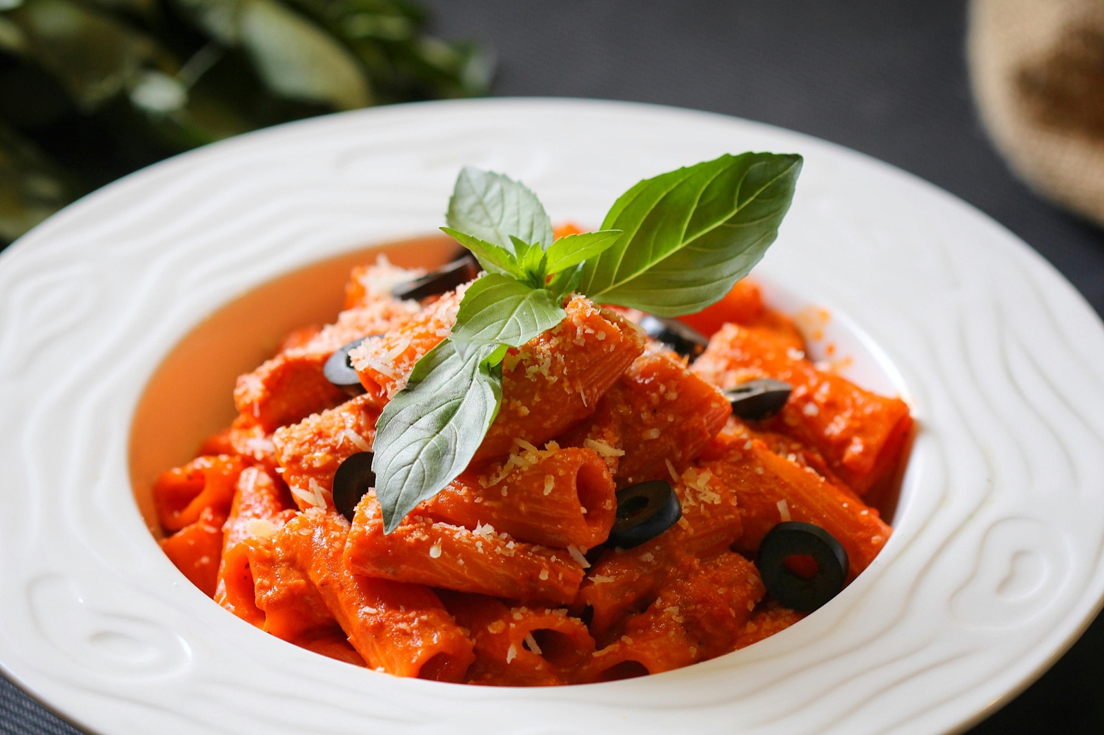 Un plato de pasta con salsa de tomate, aceitunas negras y una hoja de albahaca fresca, servido en un plato blanco